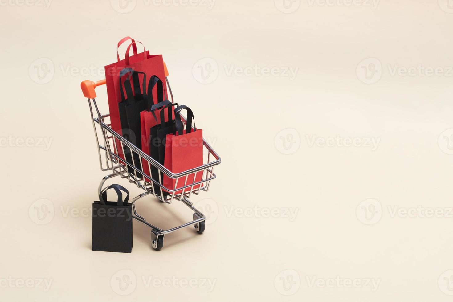 Black Friday-Konzept, Mockup von schwarzen und roten Einkaufstüten aus Papier mit Trolley auf farbigem Hintergrund. Verkauf am schwarzen Freitag. foto