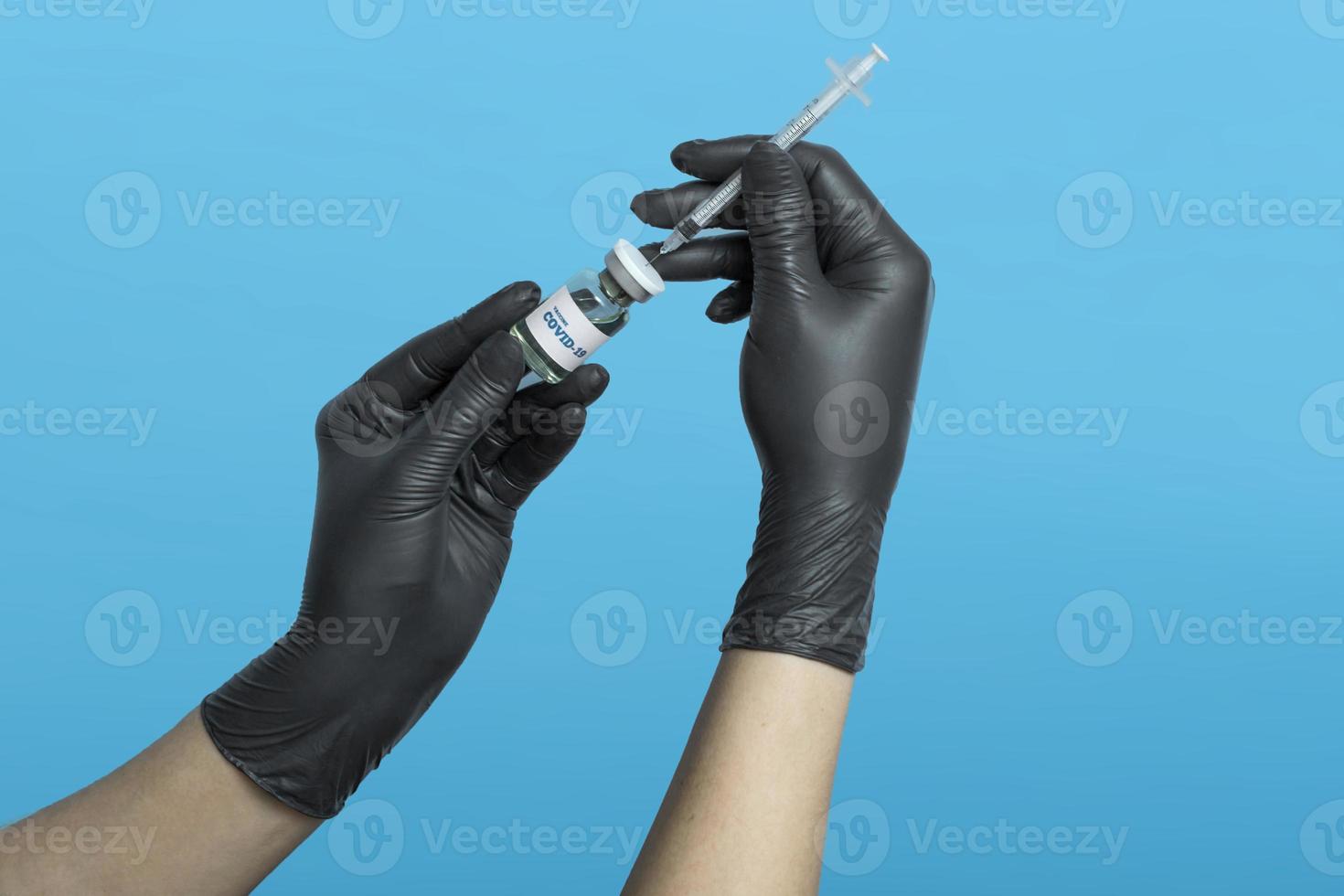 Impfkonzept. Entwicklung und Herstellung eines Impfstoffs gegen das Coronavirus. medizinisches Konzept auf blauem Hintergrund. Die Hände des Arztes in schwarzen medizinischen Handschuhen mit einer Spritze und einem Covid-19-Impfstoff. foto