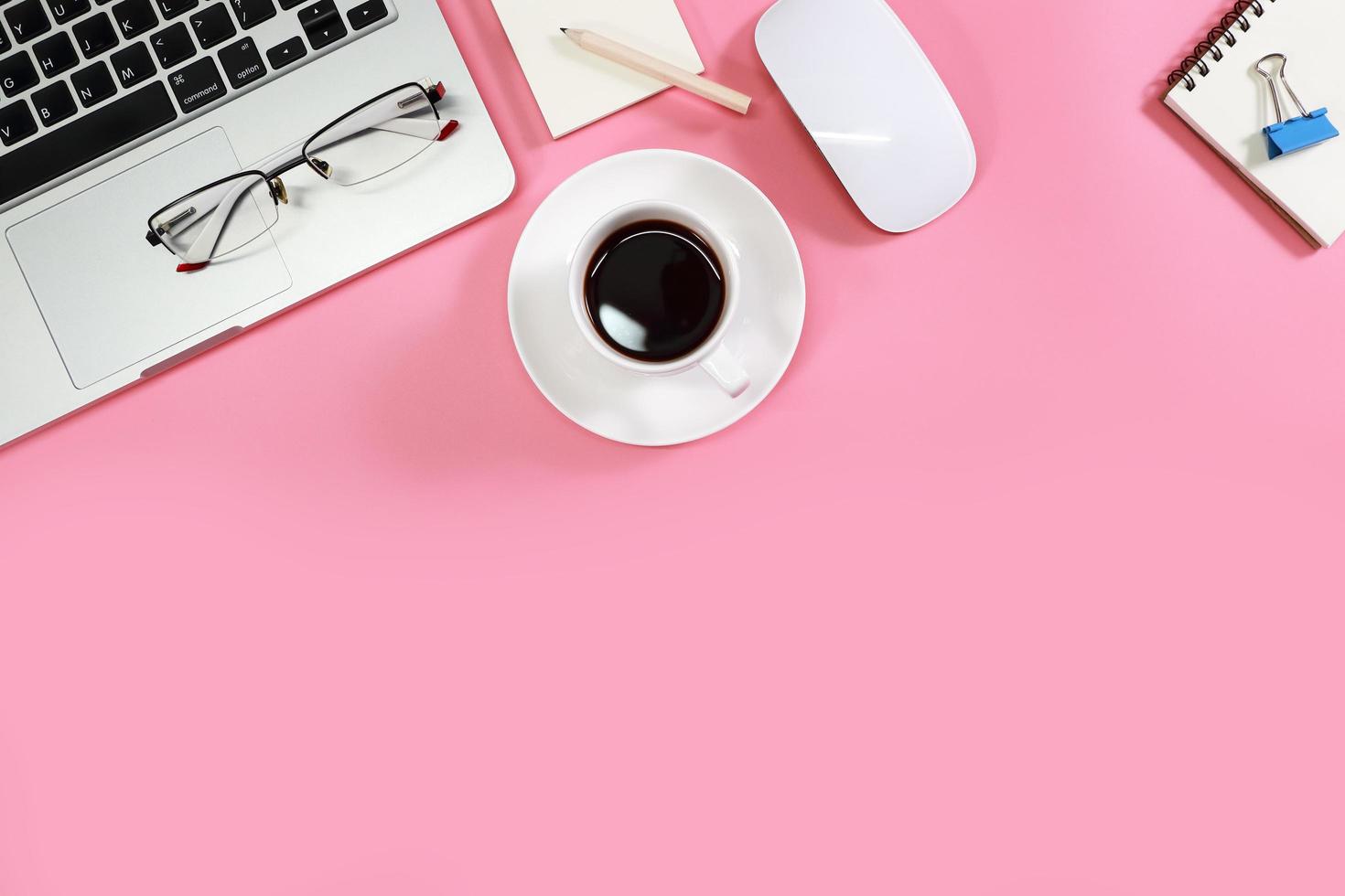 Flacher Arbeitstisch mit Laptop, Bürobedarf, Kaffeetasse, Handy, Tablet und Kaffeetasse auf rosa Hintergrund foto