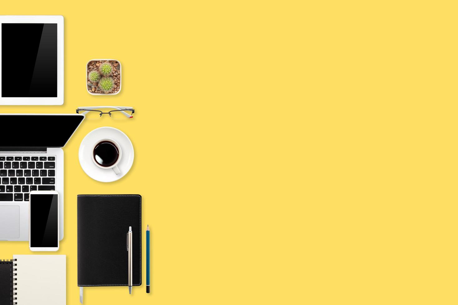 Flacher Arbeitstisch mit Laptop, Bürobedarf, Kaffeetasse, Tablet und Handy auf gelbem Pastellhintergrund foto