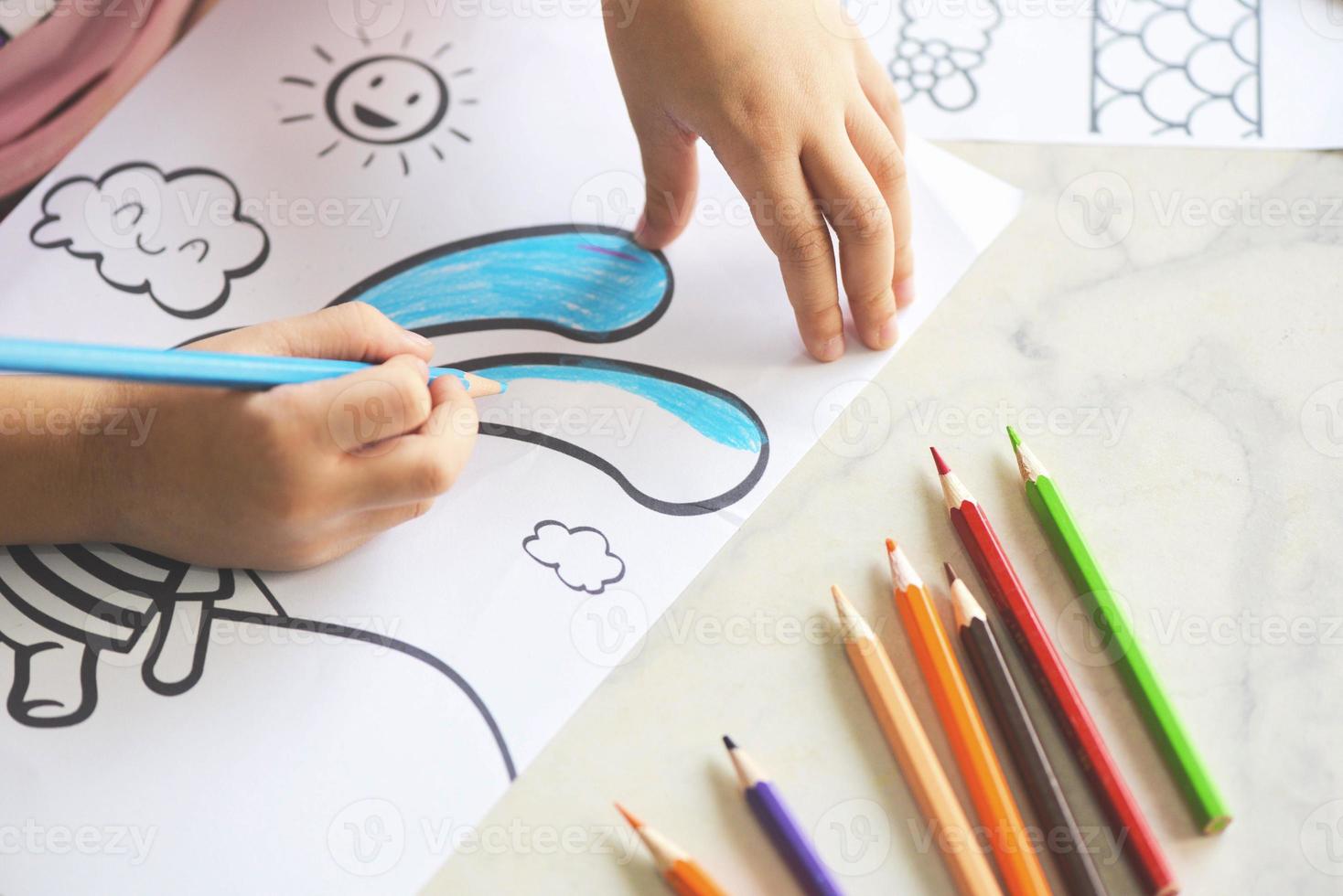Kindermädchen malen auf Papierblatt mit Farbstiften auf dem Holztisch zu Hause - lernen Sie das Kind beim Zeichnen von Bildern und bunten Buntstiften foto