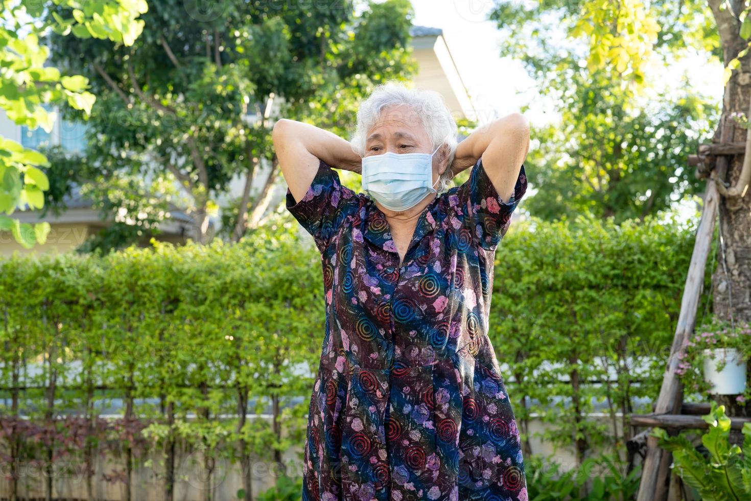 Asiatische Seniorin mit Maske schützt Coronavirus-Übungen mit glücklichem Park, gesundem, starkem medizinischem Konzept foto