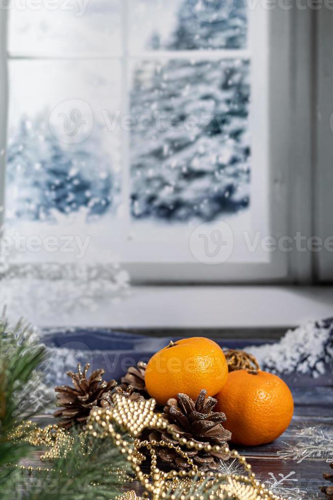 Mandarinen auf grauem Hintergrund mit Zweigen eines Weihnachtsbaumes, im Hintergrund ein Fenster mit Schnee. neues Jahr Konzept. foto
