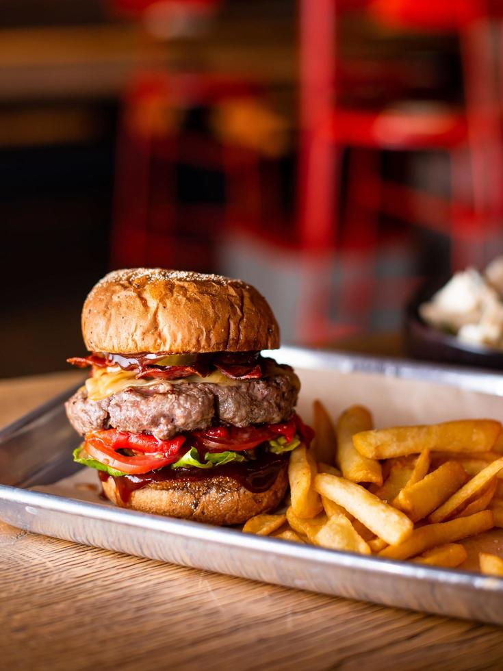 Leckerer gegrillter Burger mit Rindfleisch, Käse, Speck und Sauce auf Holztisch mit Pommes frites und Bier foto