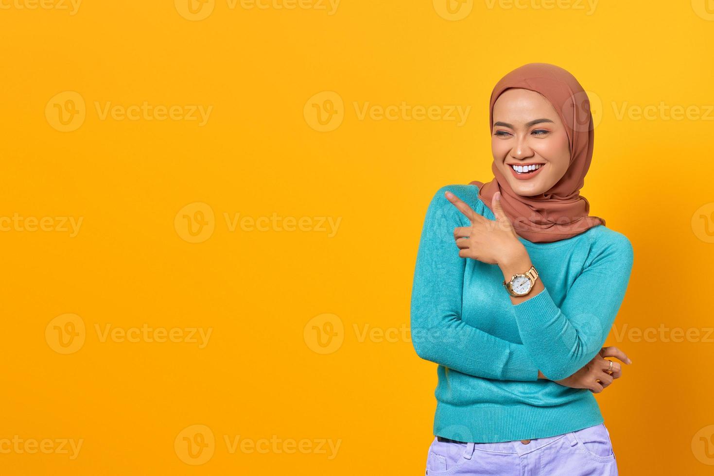 Porträt einer lächelnden jungen Asiatin, die mit dem Finger auf den Kopierraum auf gelbem Hintergrund zeigt foto