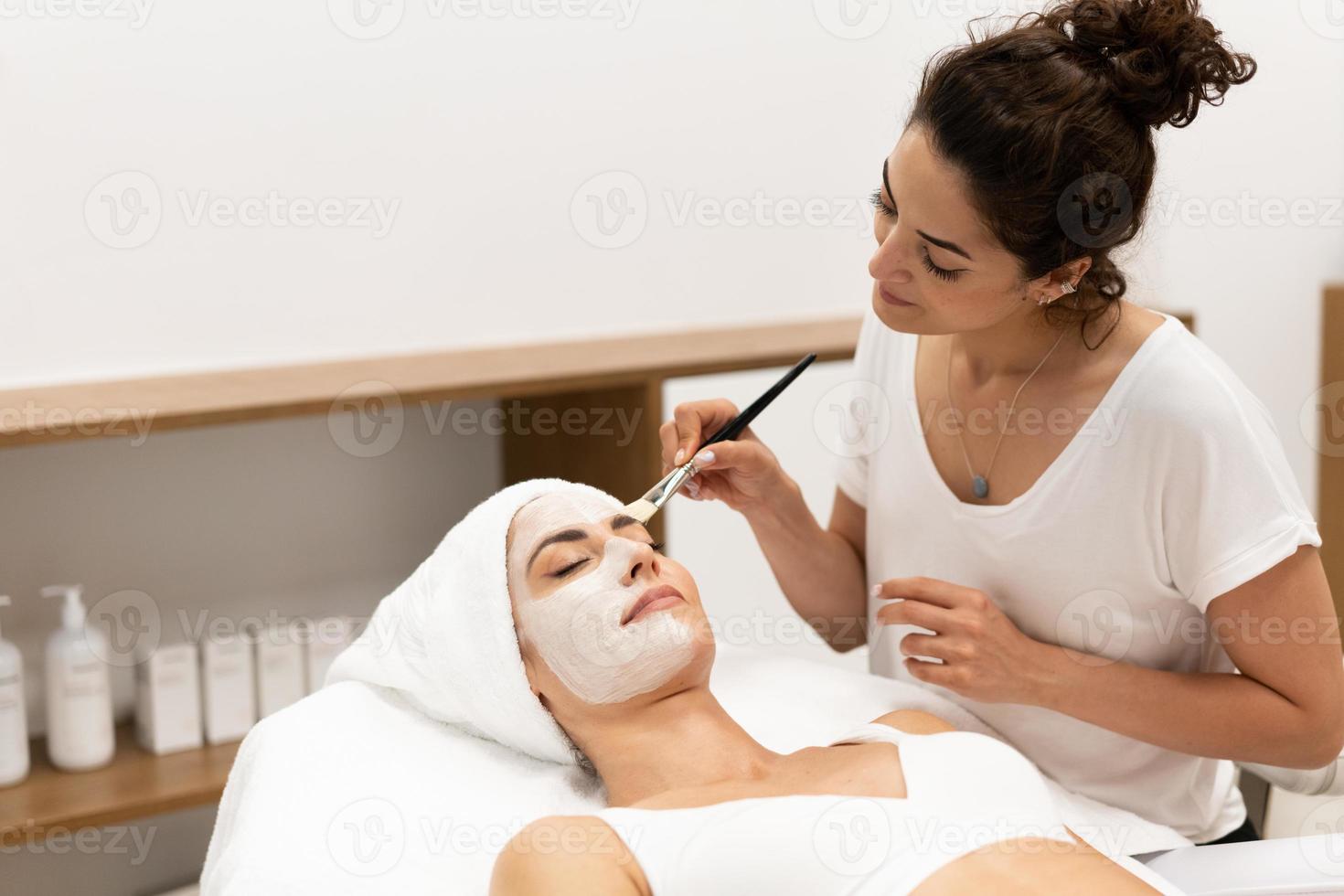 Ästhetik, die in einem modernen Wellnesscenter eine Maske auf das Gesicht einer Frau mittleren Alters aufträgt. foto