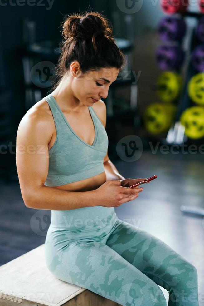 Frau, die ihr Training auf ihrem Smartphone bespricht, sitzt in einer Sprungbox foto