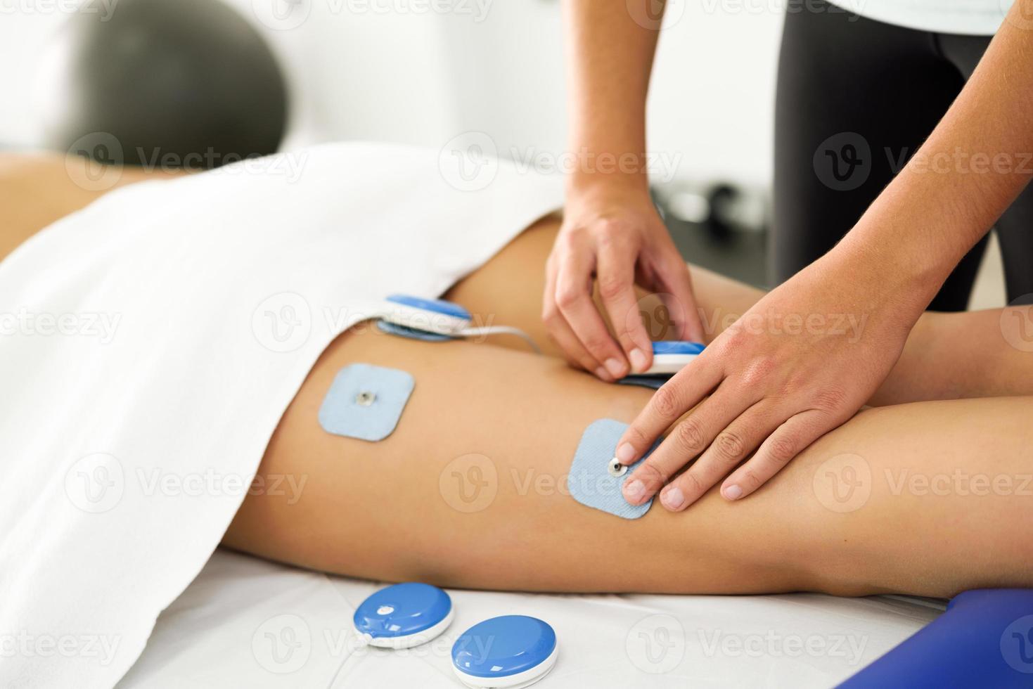 Physiotherapeut, der Elektrostimulation in der Physiotherapie an einem Bein einer jungen Frau anwendet. foto