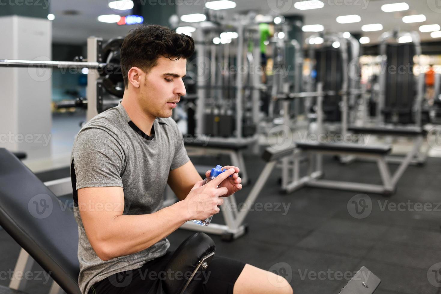 hübscher junger Mann in Sportkleidung mit Wasserflasche im Fitnessstudio foto