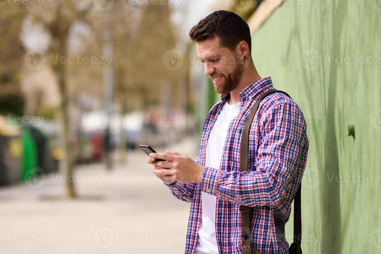 lächelnder junger Mann, der sein Smartphone im städtischen Hintergrund sucht. Lifestyle-Konzept. foto