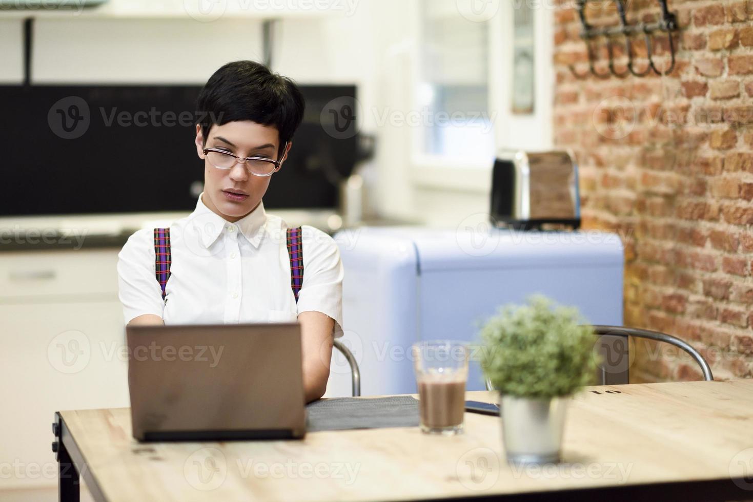 spanien, madrid, madrid. junge Frau mit sehr kurzem Haarschnitt, die zu Hause mit einem Laptop tippt. Arbeiten zu Hause Konzept. foto