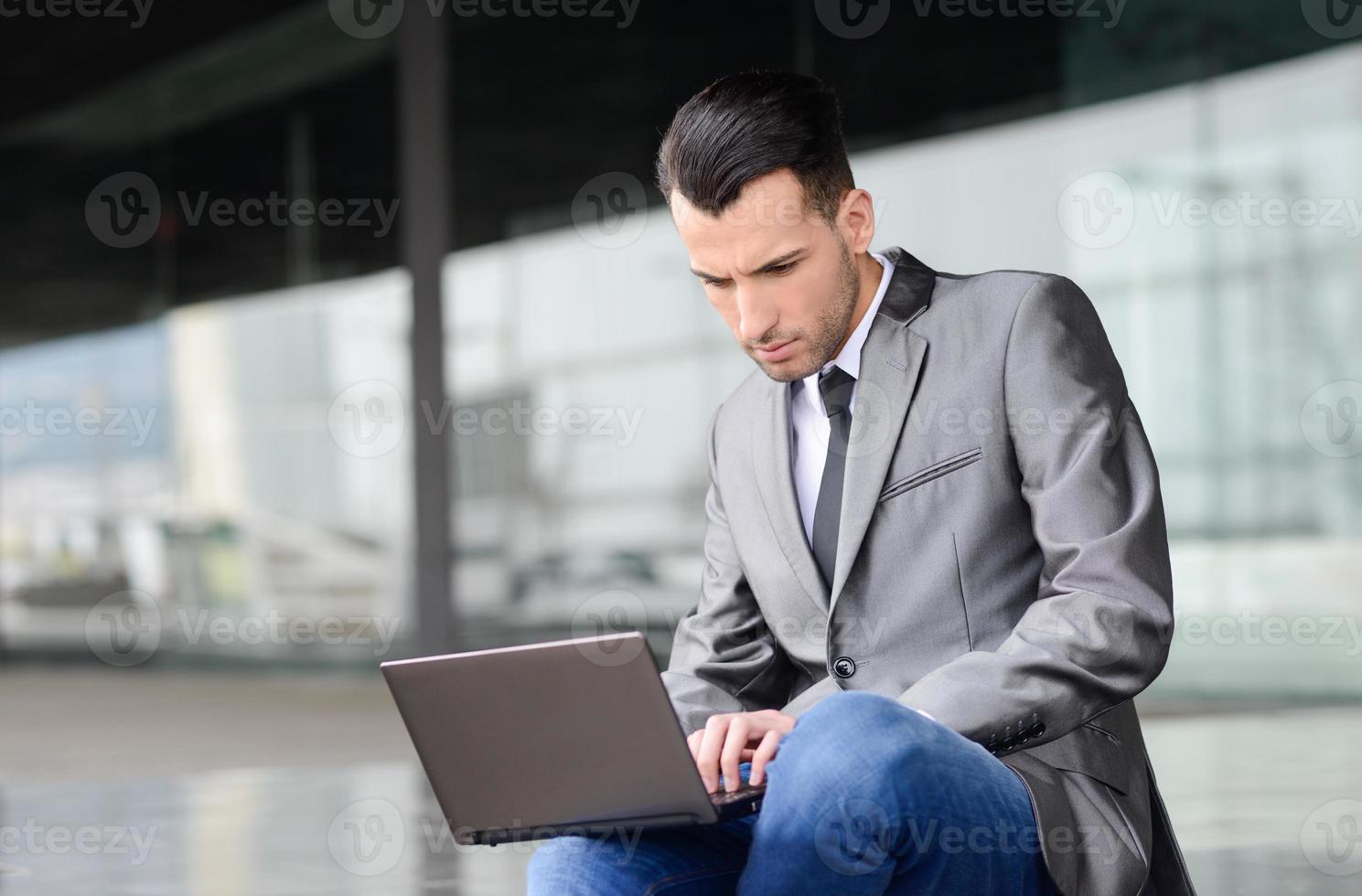 junger Geschäftsmann, der einen Laptop im städtischen Hintergrund eintippt foto