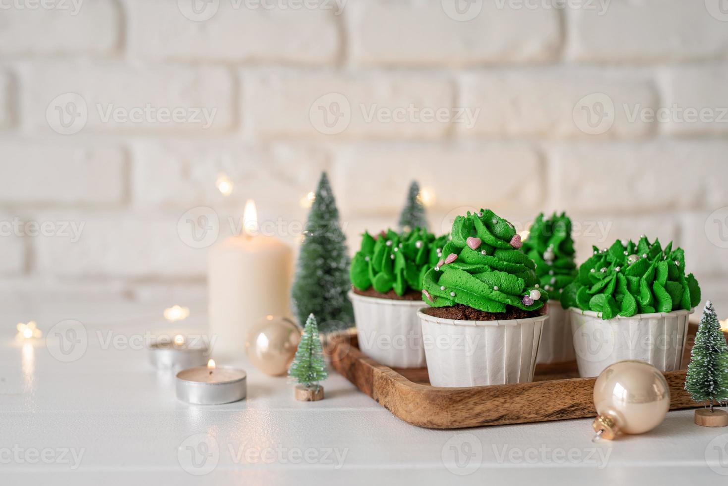 weihnachtsbaumförmige Cupcakes, umgeben von festlichen Dekorationen und Lichtern im Hintergrund foto