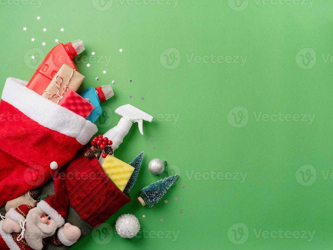 Reinigungswerkzeuge und Weihnachtsdekorationen in Santa Hut Draufsicht flach auf grünem Hintergrund mit Kopienraum lagen foto