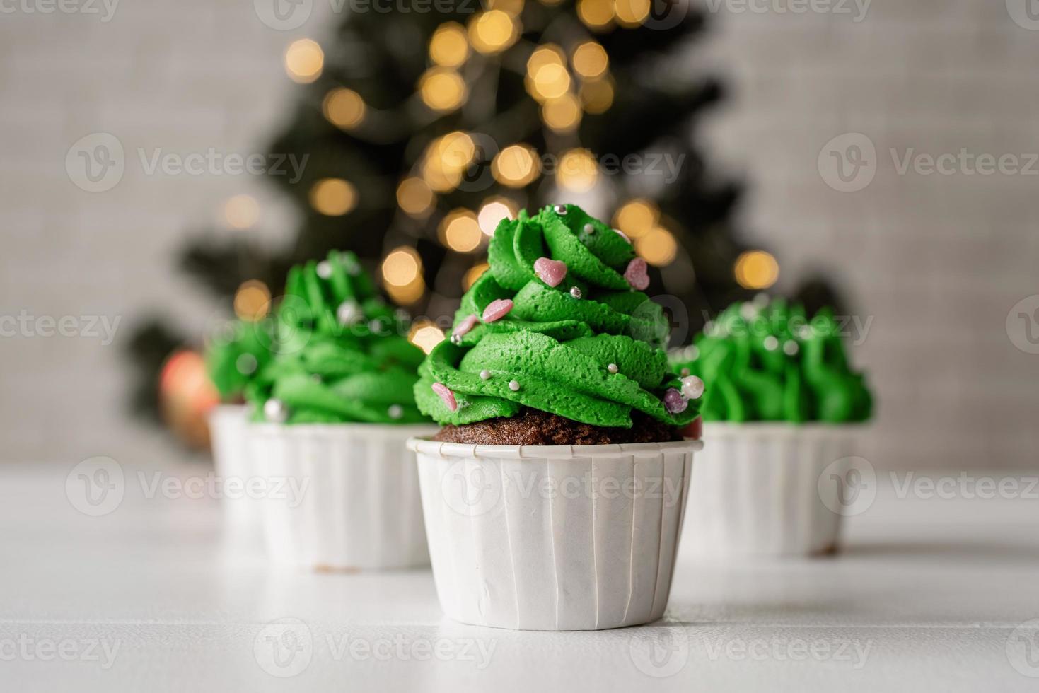 weihnachtsbaumförmige Cupcakes, umgeben von festlichen Dekorationen und Lichtern im Hintergrund foto