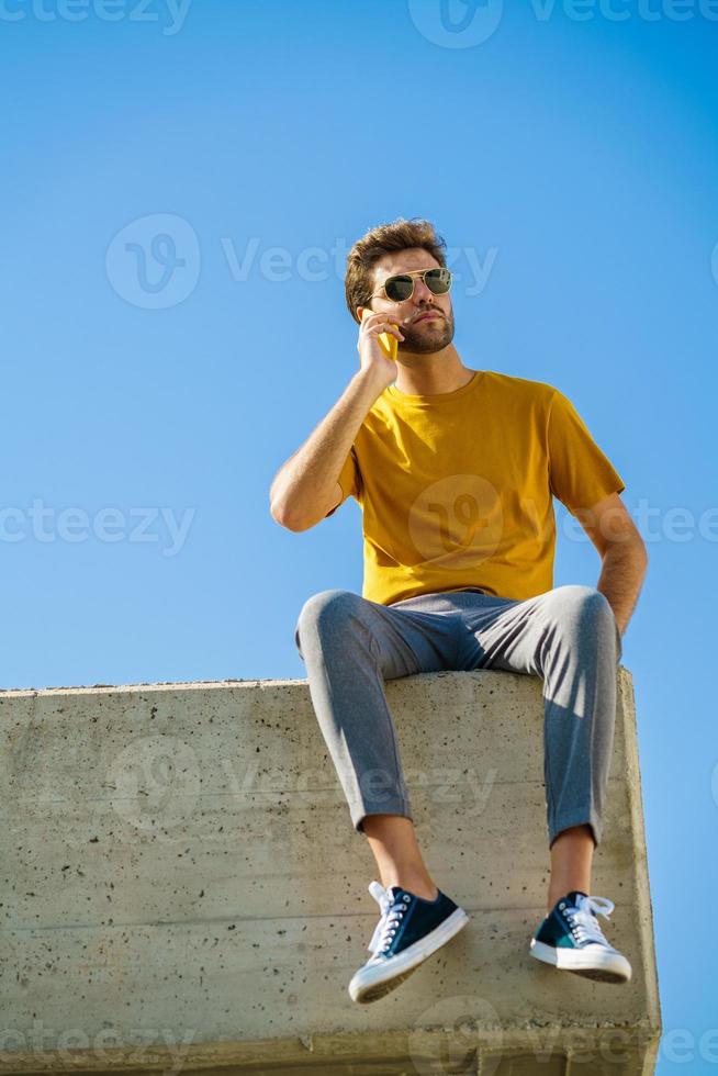 junger Mann mit seinem Smartphone draußen auf einem Felsvorsprung sitzend foto