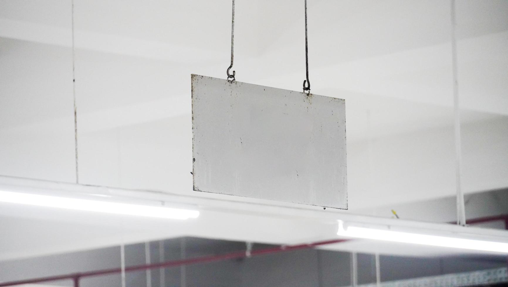 eine leere weiße Tafel am Bahnhof, die mit Eisen auf dem Dach hängt. schmutzig und ein wenig rostig. ein leeres Zeug für einen Kopienraum oder sonst. foto