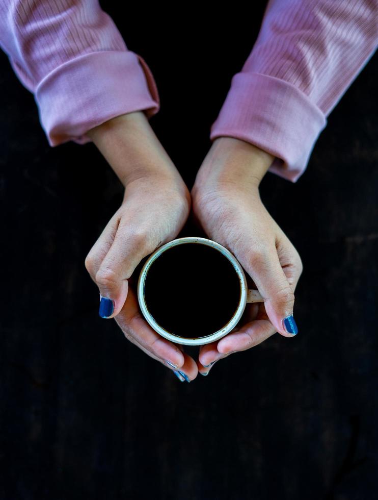 Auf dem Tisch steht eine Tasse heißen Kaffee. Ein Mädchen hält ein leckeres Getränk in der Hand. eine Art Freizeitvergnügen. foto