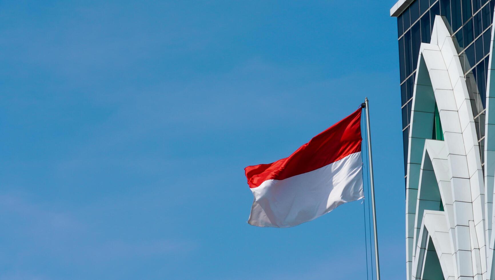 die indonesische flagge weht hoch. die wehende Fahne vor einem Gebäude. die rot-weiße Flagge weht stolz an einem sonnigen Tag. foto