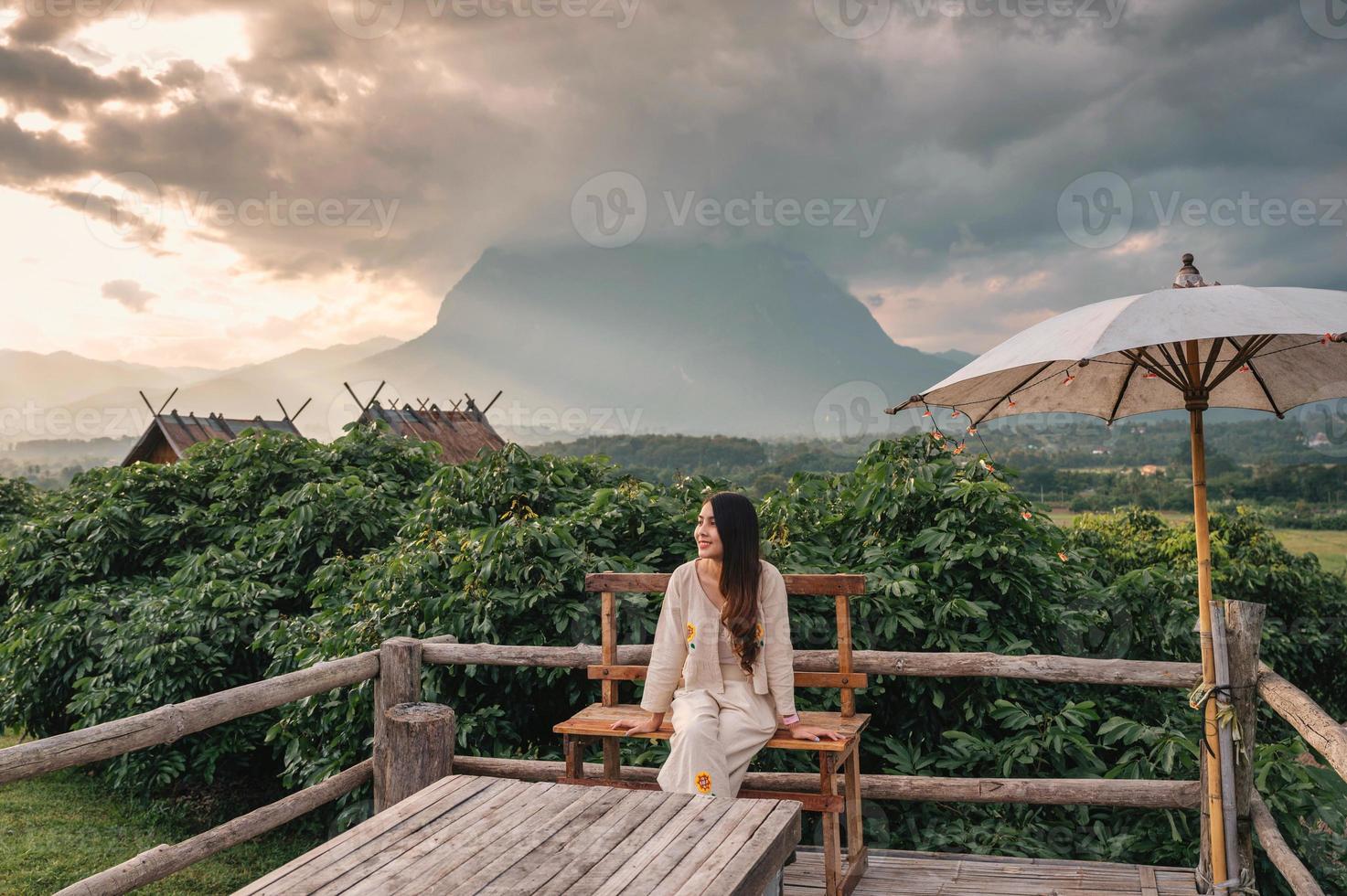 junge asiatische frau sitzt auf der terrasse und blick auf die berge von doi luang chiang dao im sonnenuntergang foto