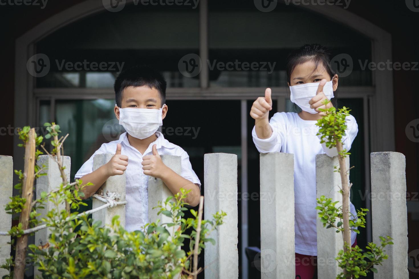 asiatische Kinder, die eine Schutzmaske tragen, die innerhalb des Hauszauns steht foto