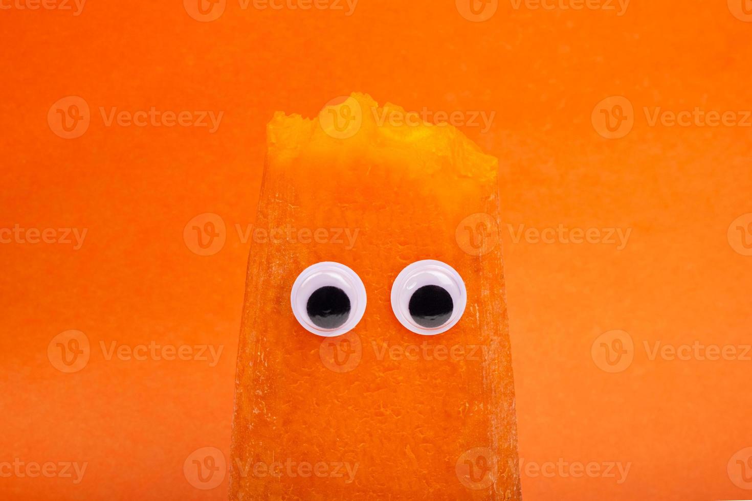 Karotte mit Augen auf orangem Hintergrund, Gemüsegesicht foto