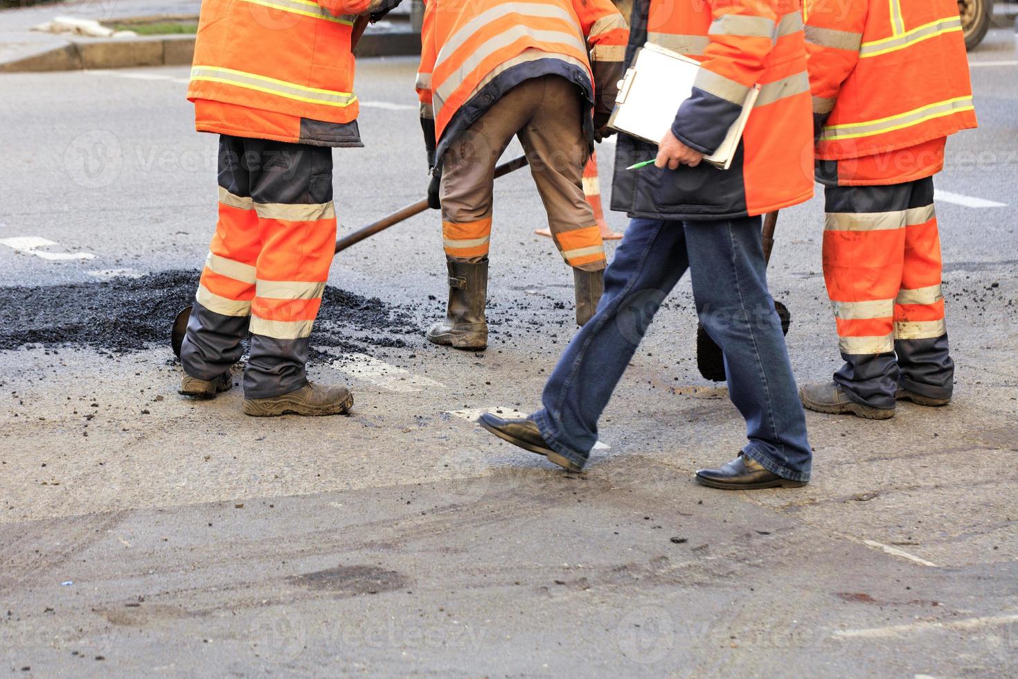 ein team von straßenbauern sammelt und fluchtet mit einer schaufel frischen asphalt entlang des reparierten straßenteils. foto