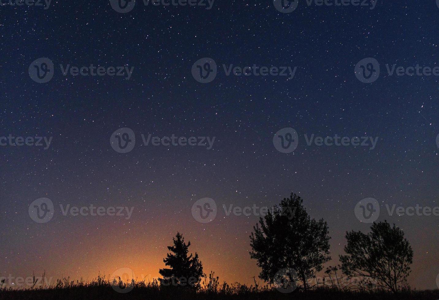 Silhouetten von drei Bäumen vor dem Hintergrund des nächtlichen Sternenhimmels und der untergehenden Sonne foto