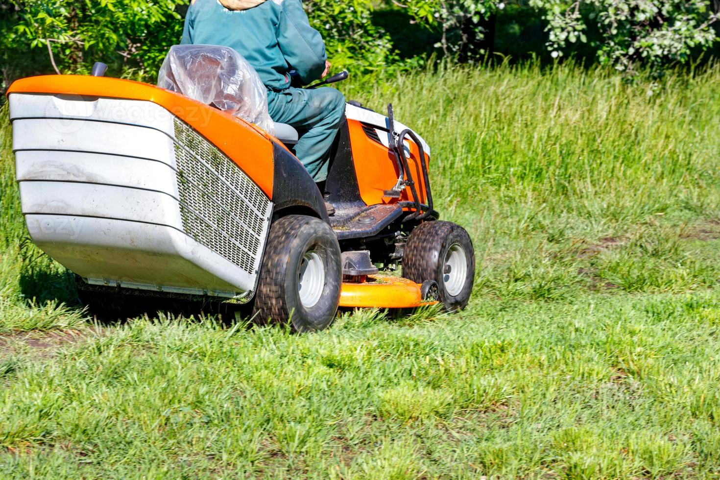 Grüner Rasen und professioneller Traktor-Rasenmäher an einem klaren, sonnigen Tag. foto