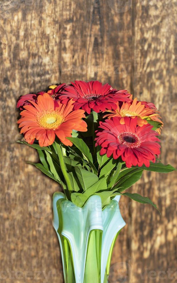 schöner Strauß Gerberas in einer glasfarbenen Vase auf dem Hintergrund einer alten Vintage-Holzwand foto