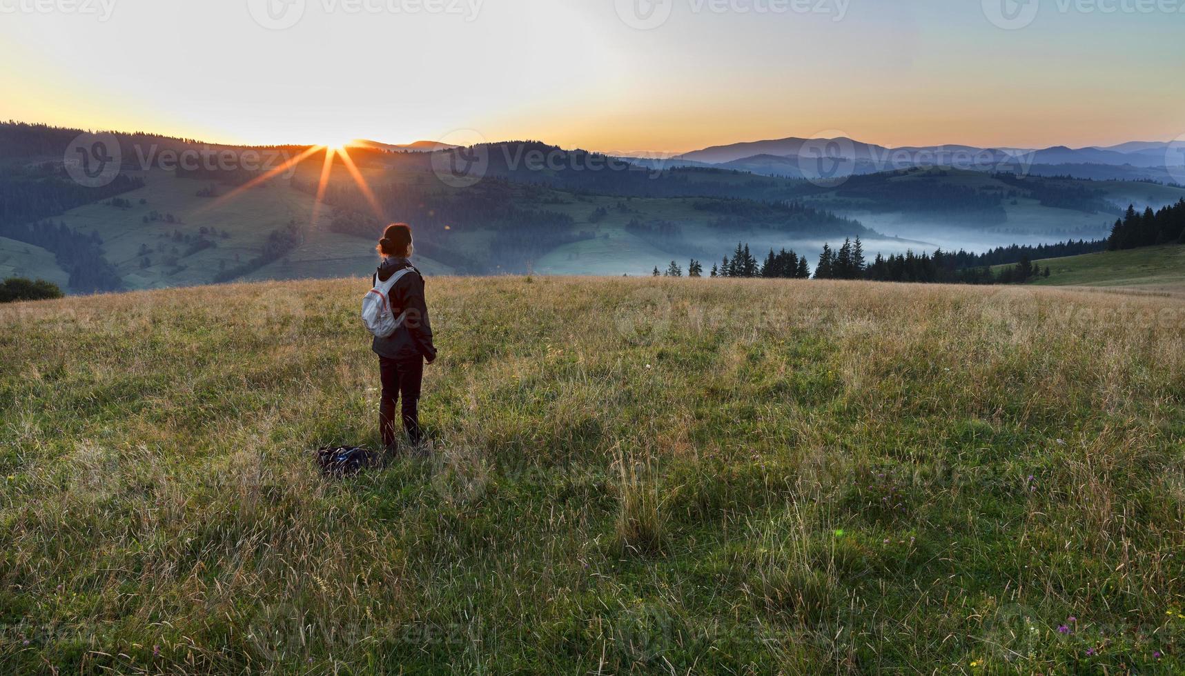 auf einem Wiesenhügel in den Karpaten trifft eine junge Frau auf eine Morgendämmerung foto