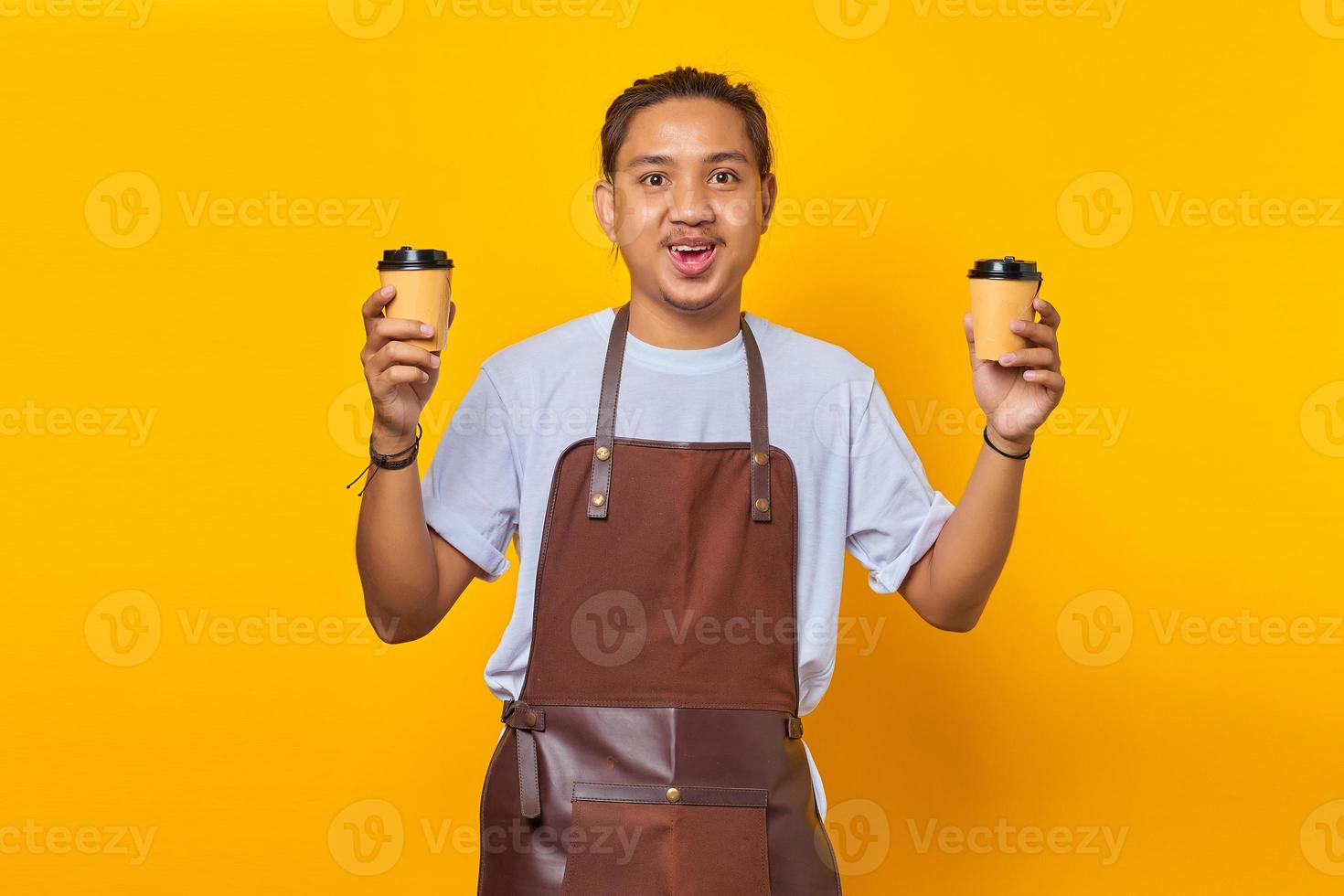 Porträt eines fröhlichen Barista-Mannes, der zwei Kaffeetassen aus Papier hält, die Sie einzeln auf gelbem Hintergrund auswählen können foto