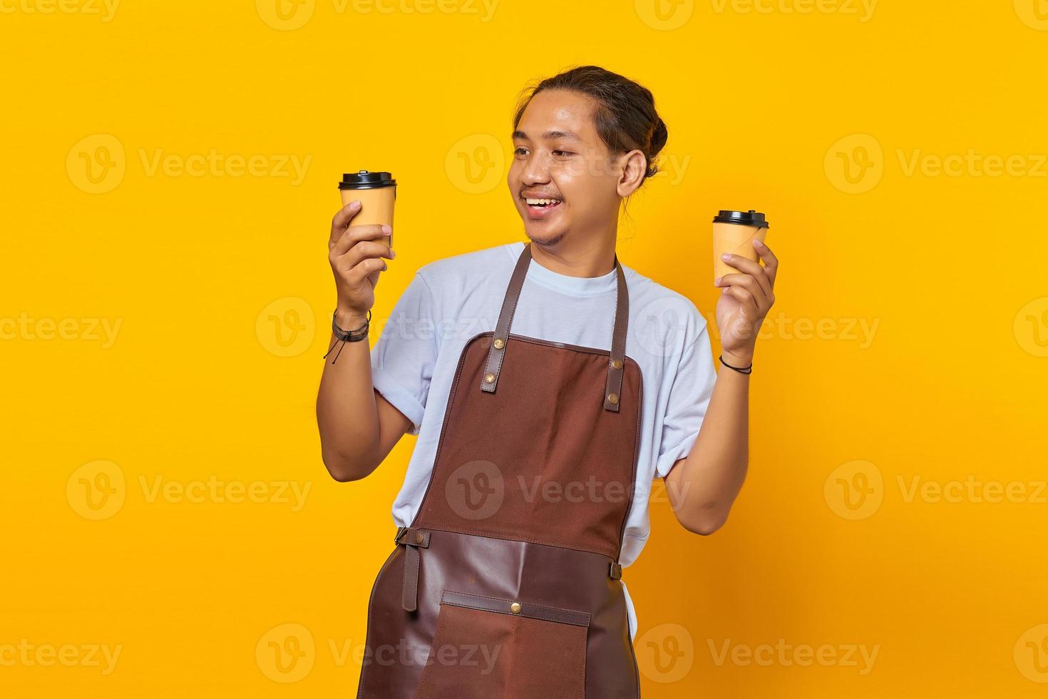 Porträt eines fröhlichen Barista-Mannes, der zwei Kaffeetassen aus Papier hält, die Sie einzeln auf gelbem Hintergrund auswählen können foto