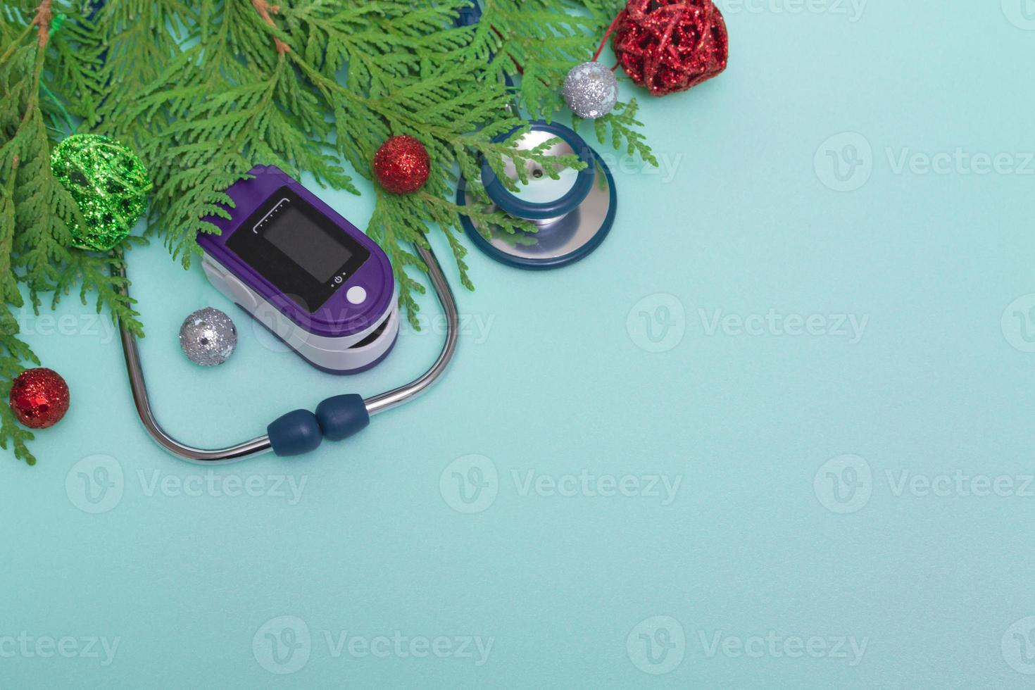 medizinisches Konzept, das Weihnachten im Gesundheitswesen feiert. Draufsicht auf eine flache Lage Nahaufnahme eines Stethoskops, Pulsoximeter mit Tannenzweigen auf grünem Hintergrund, Kopierraum. foto