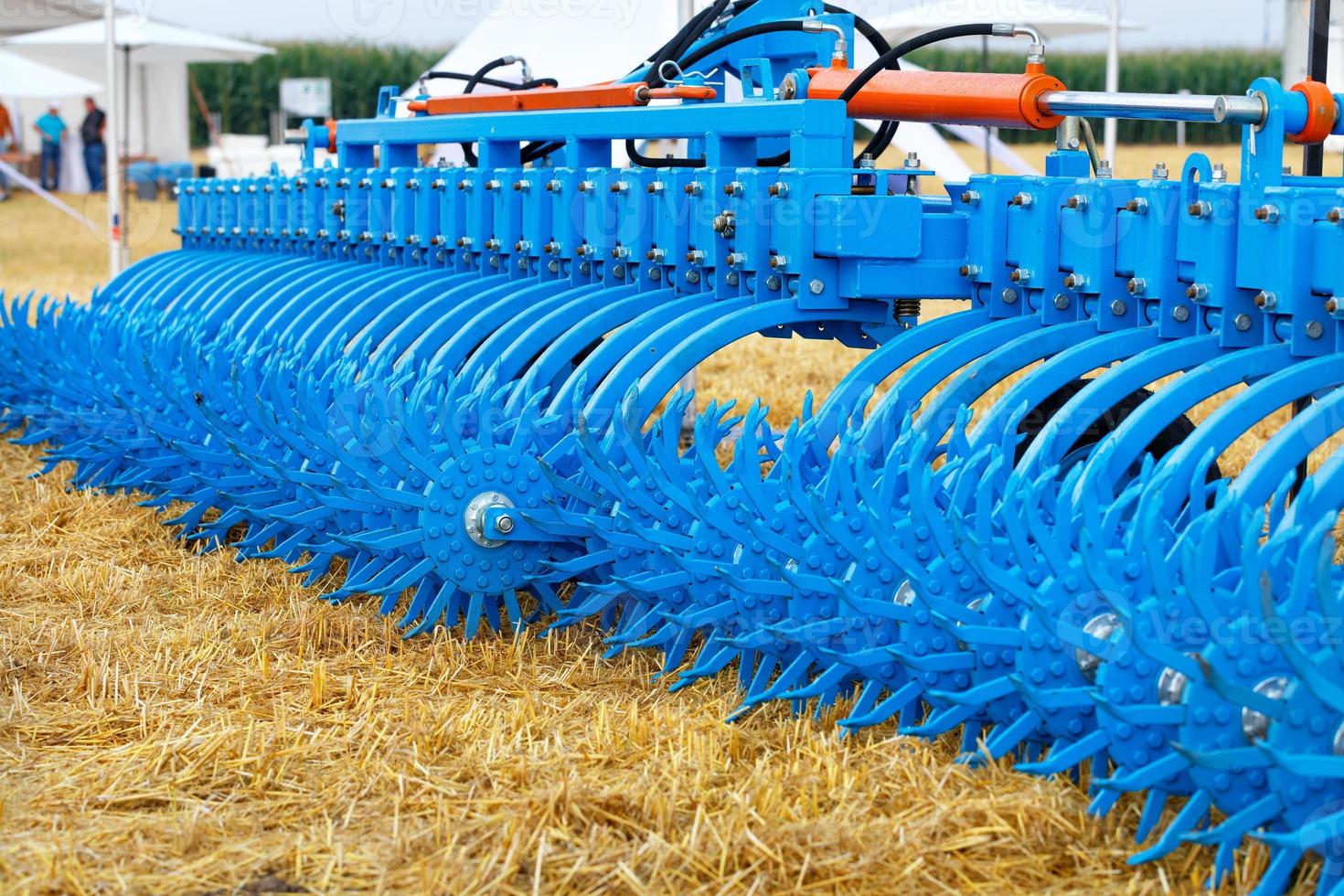 eine mehrreihige gezahnte Metallegge von blauer Farbe vor dem Hintergrund eines abgeernteten gelben Feldes, Nahaufnahme. foto