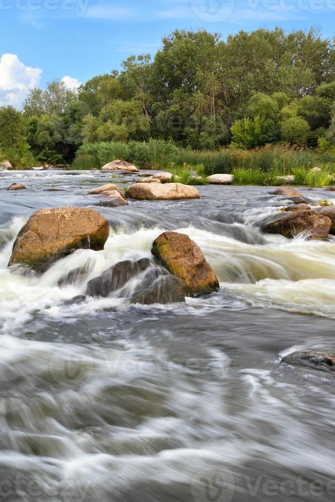 stürmische Wasserströme, die an einem hellen Sommertag felsige Stromschnellen überwinden, vertikale Aufnahme. foto