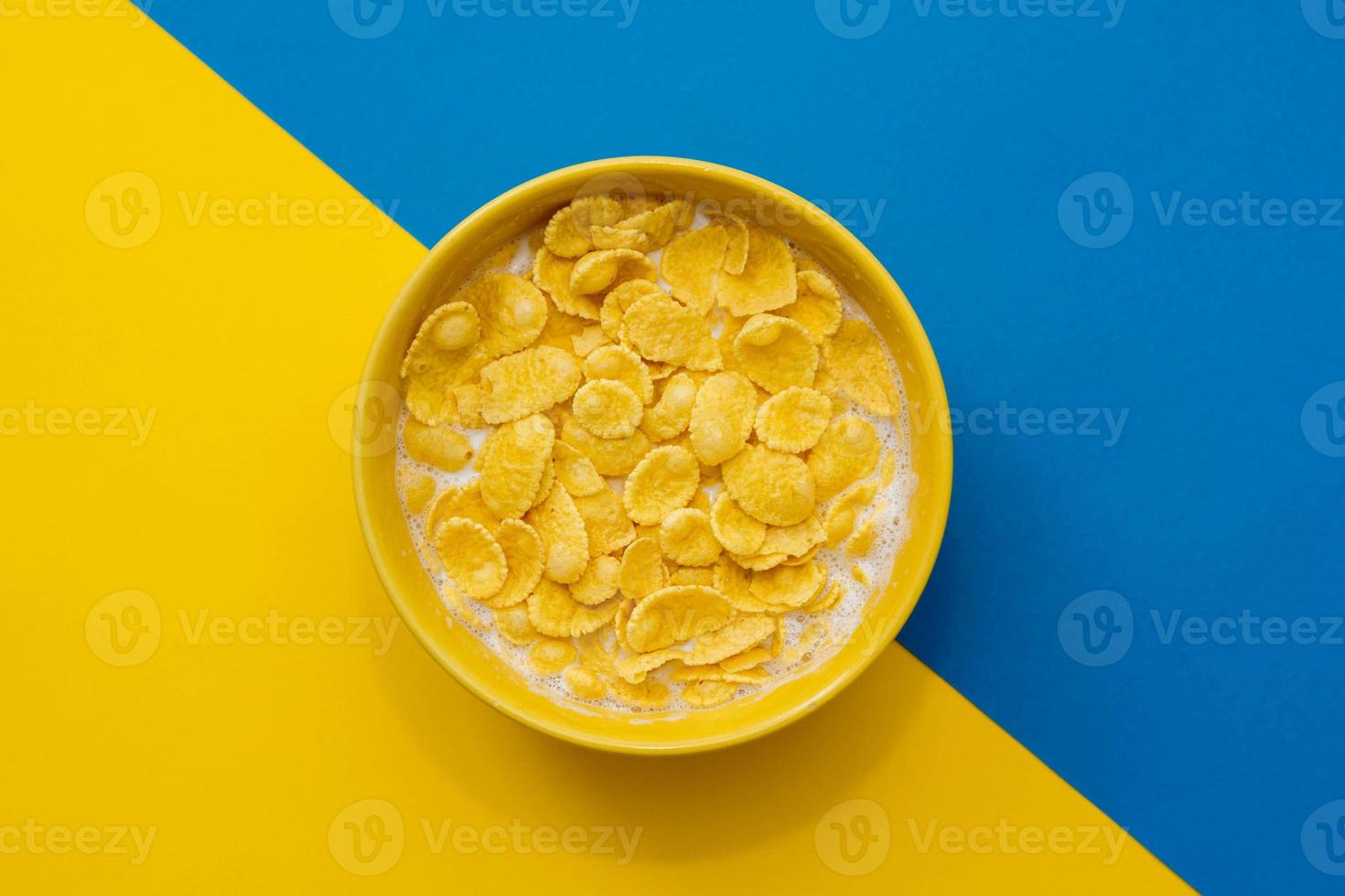 Cornflakes mit Milch in der gelben Schüssel auf blauem und gelbem Hintergrund foto