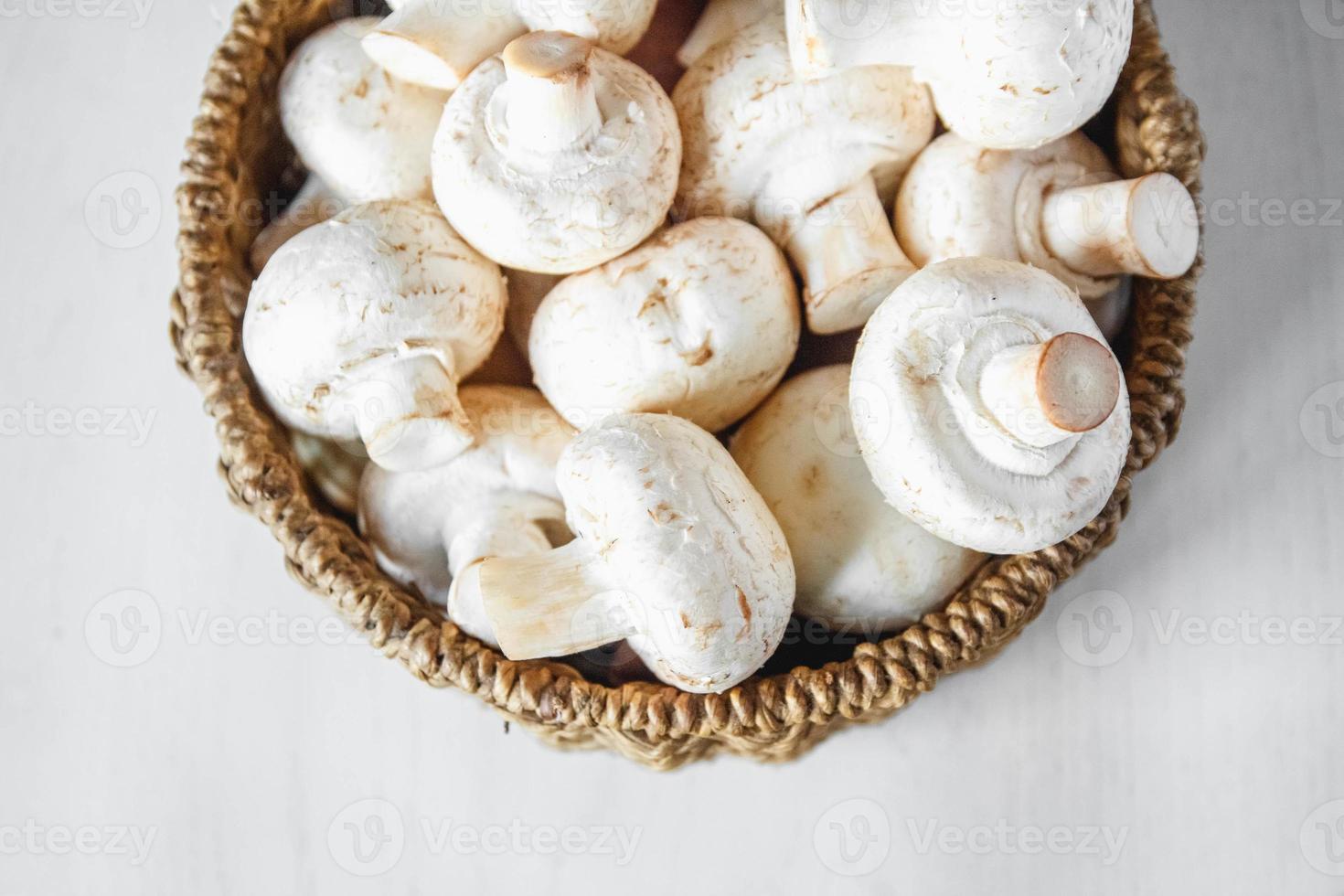 Champignons Champignons in einem runden Weidenkorb auf einem weißen Holztisch foto