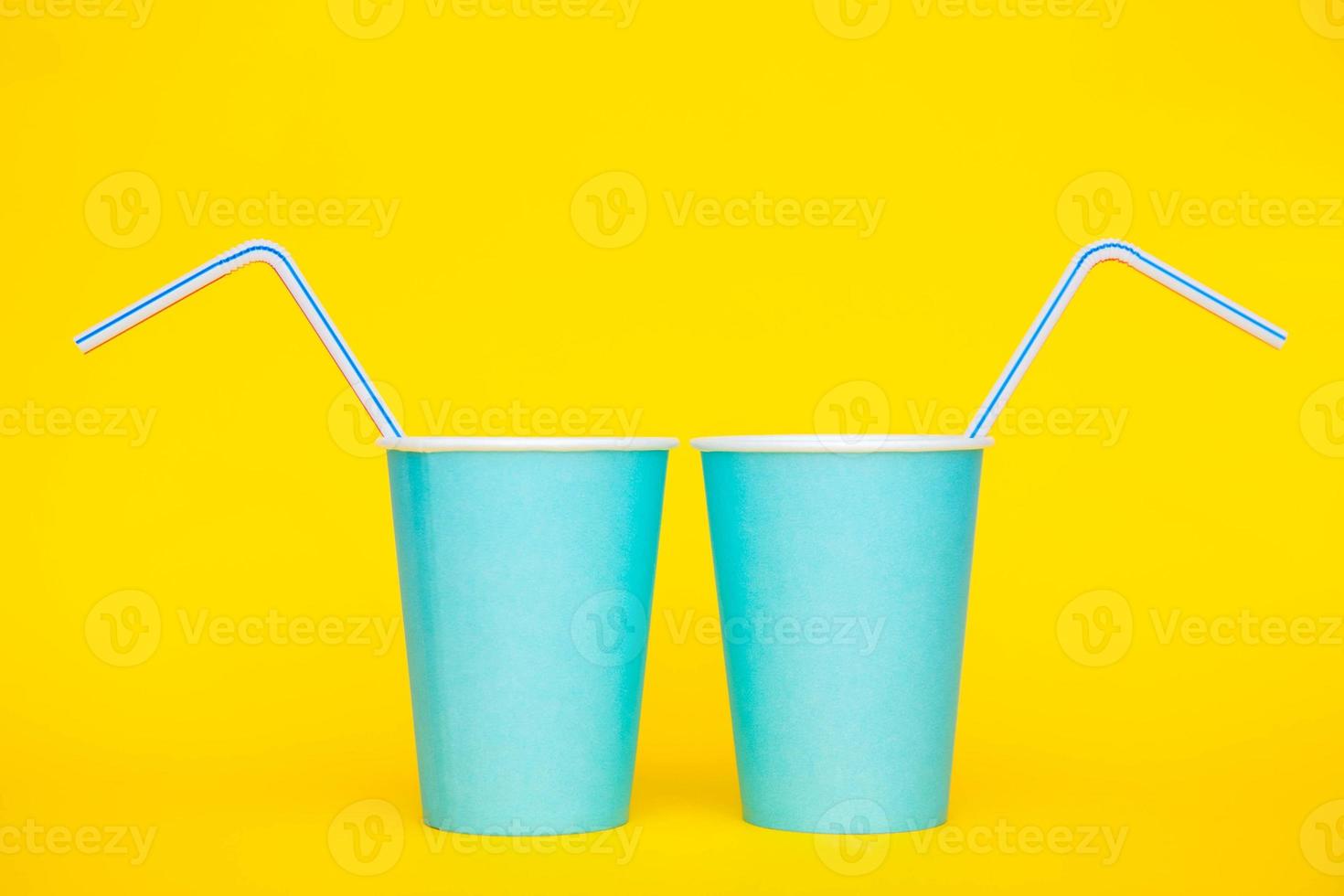 zwei blaue Pappbecher mit Trinkhalmen aus farbigem Plastik auf gelbem Hintergrund foto