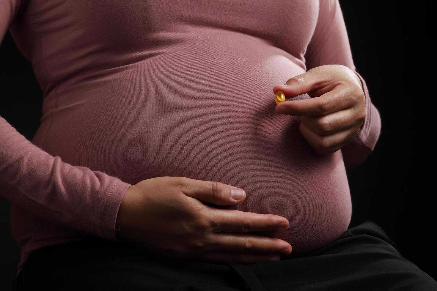 Nahaufnahme schwangere Frau mit Medizin auf schwarzem Hintergrund foto