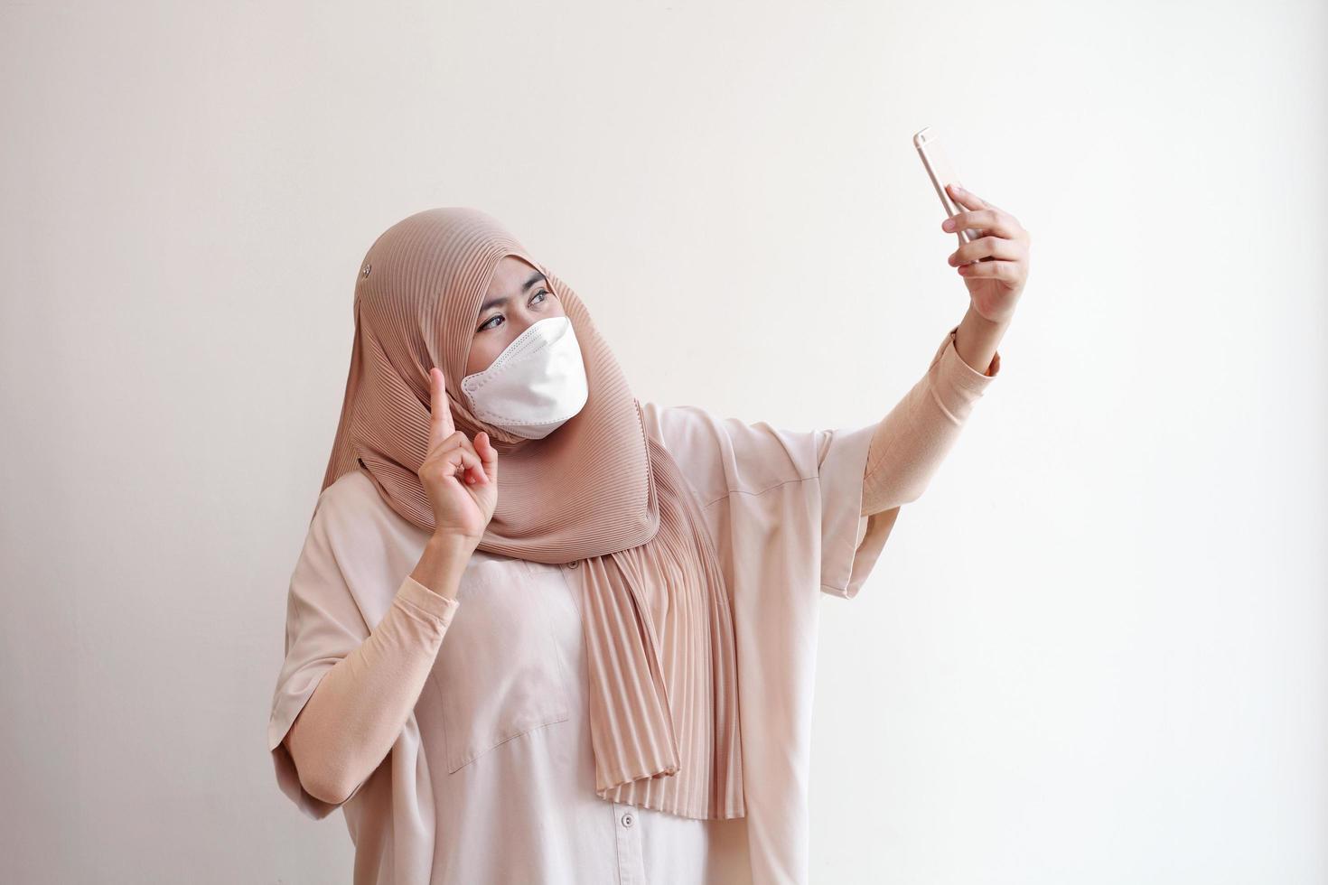 muslimisches Mädchen mit chirurgischer Maske, das ein Selfie mit dem Smartphone macht. foto