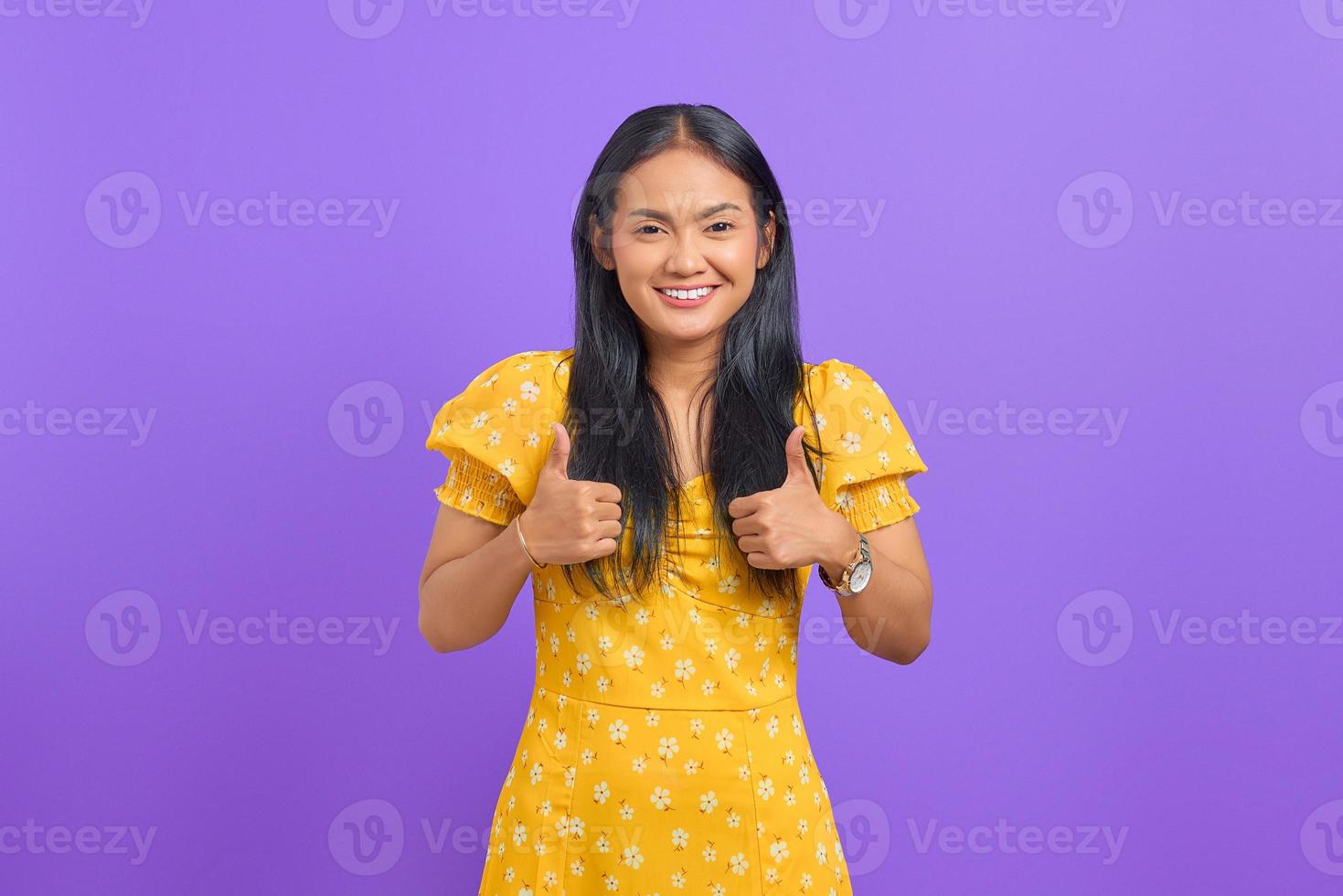Porträt einer lächelnden jungen Asiatin, die auf violettem Hintergrund Daumen in die Kamera zeigt foto