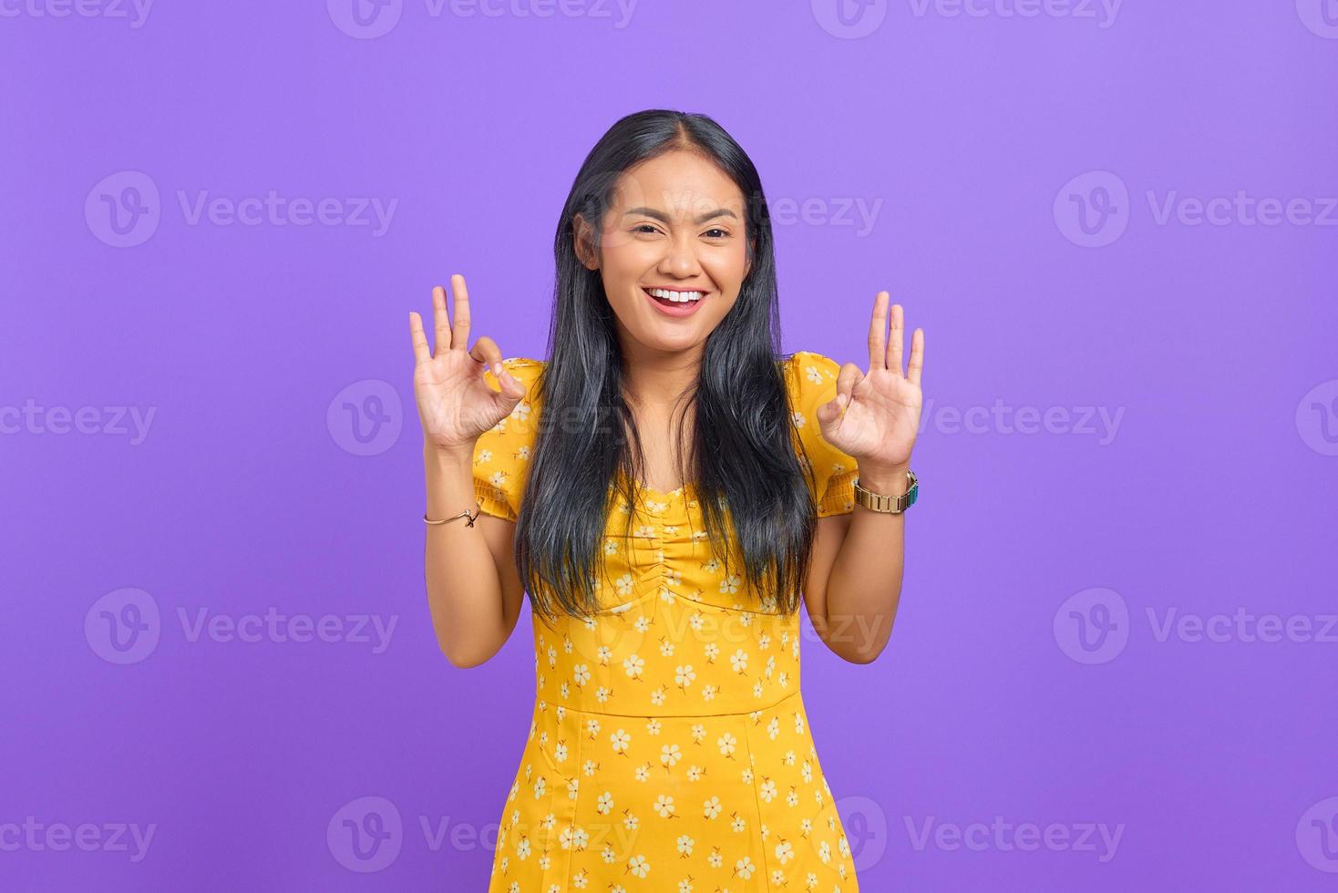 Fröhliche junge asiatische Frau macht eine gute Geste, zeigt ein Symbol der Zustimmung auf violettem Hintergrund foto