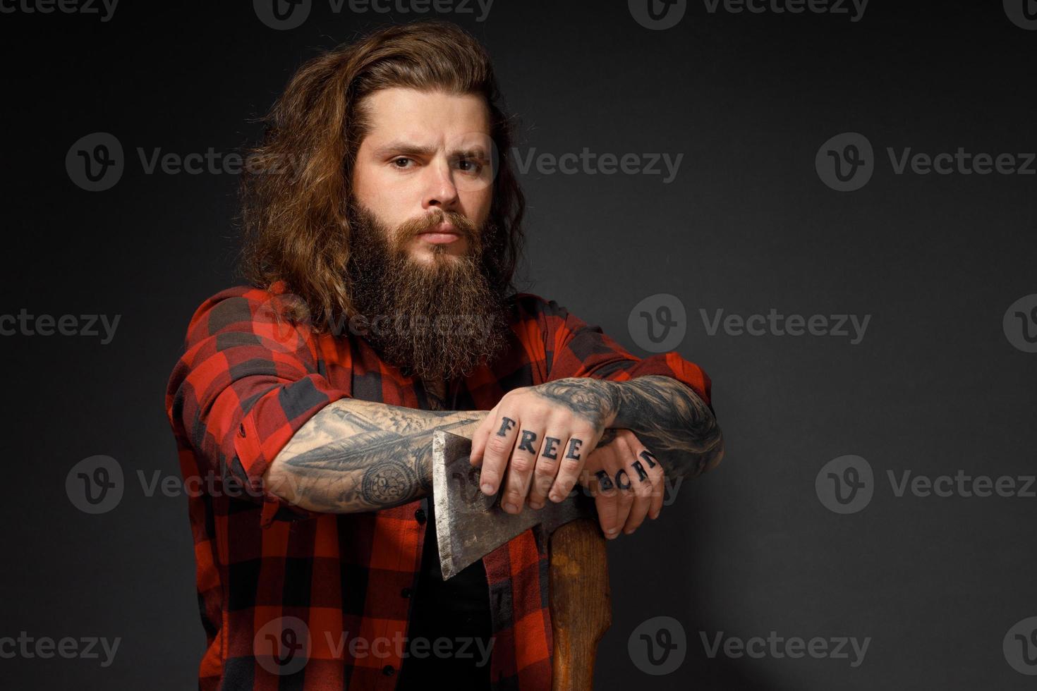 gut aussehender Mann mit langen Haaren mit einer Axt in den Händen auf dunklem Studiohintergrund foto