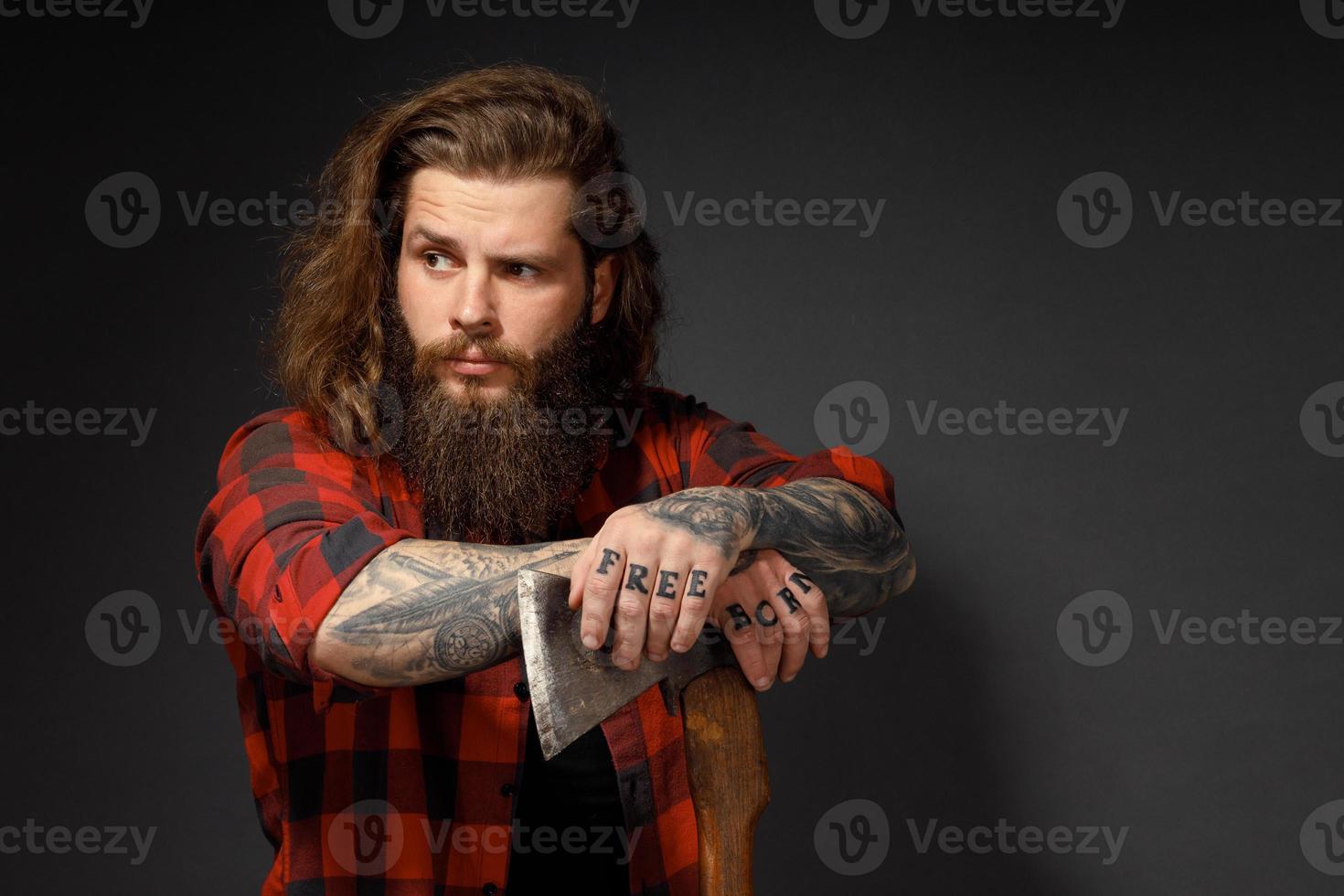 gut aussehender Mann mit langen Haaren mit einer Axt in den Händen auf dunklem Studiohintergrund foto