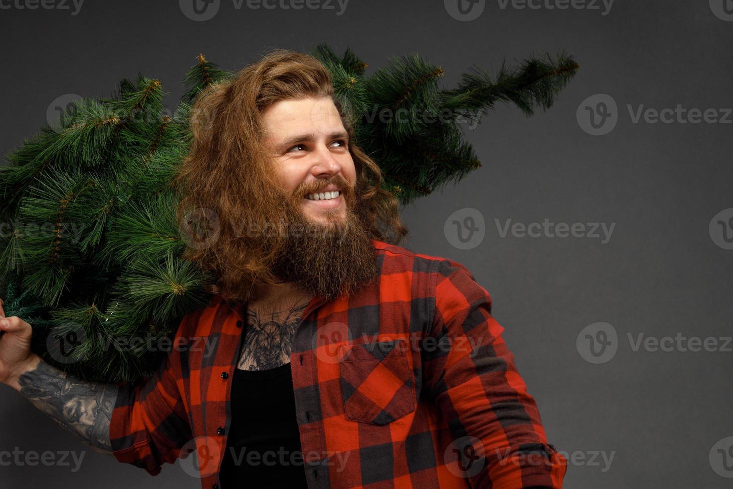 gut aussehender Mann mit langen Haaren, der einen synthetischen Weihnachtsbaum hält foto