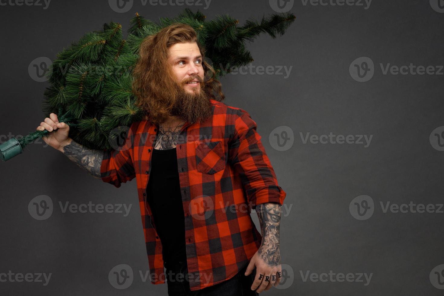 gut aussehender Mann mit langen Haaren, der einen synthetischen Weihnachtsbaum hält foto