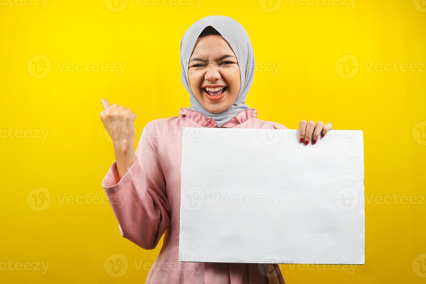 hübsche junge muslimische Frau, die fröhliche leere leere Banner, Plakate, weiße Tafeln, leere Schilder, weiße Werbetafeln hält, etwas im Kopierraum präsentiert, Werbung foto