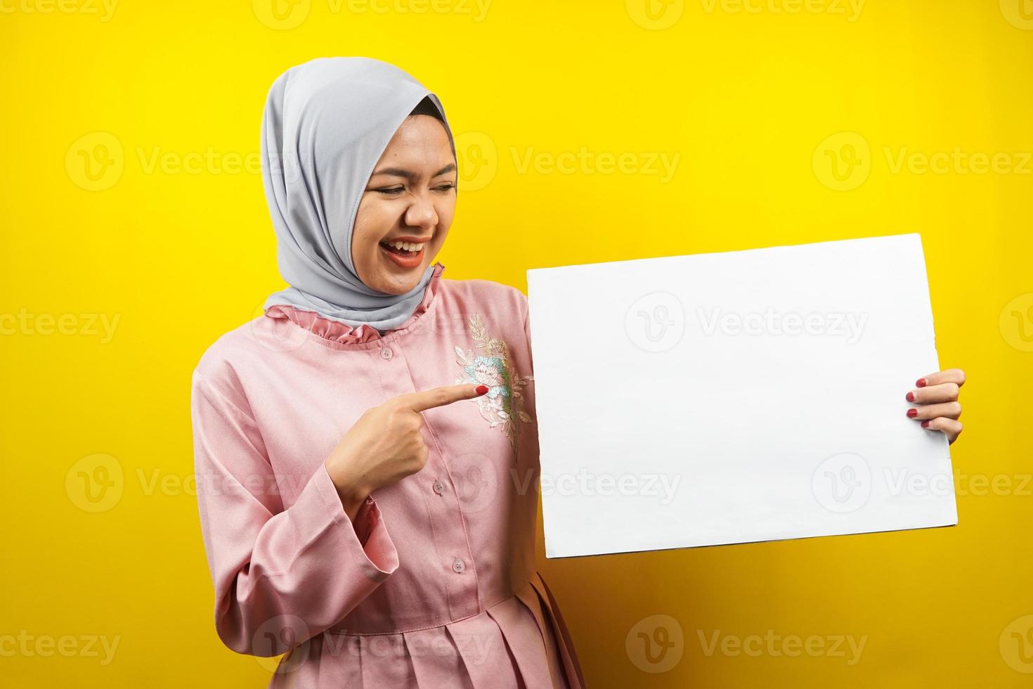 hübsche junge muslimische Frau, die fröhliche leere leere Banner, Plakate, weiße Tafeln, leere Schilder, weiße Werbetafeln hält, etwas im Kopierraum präsentiert, Werbung foto