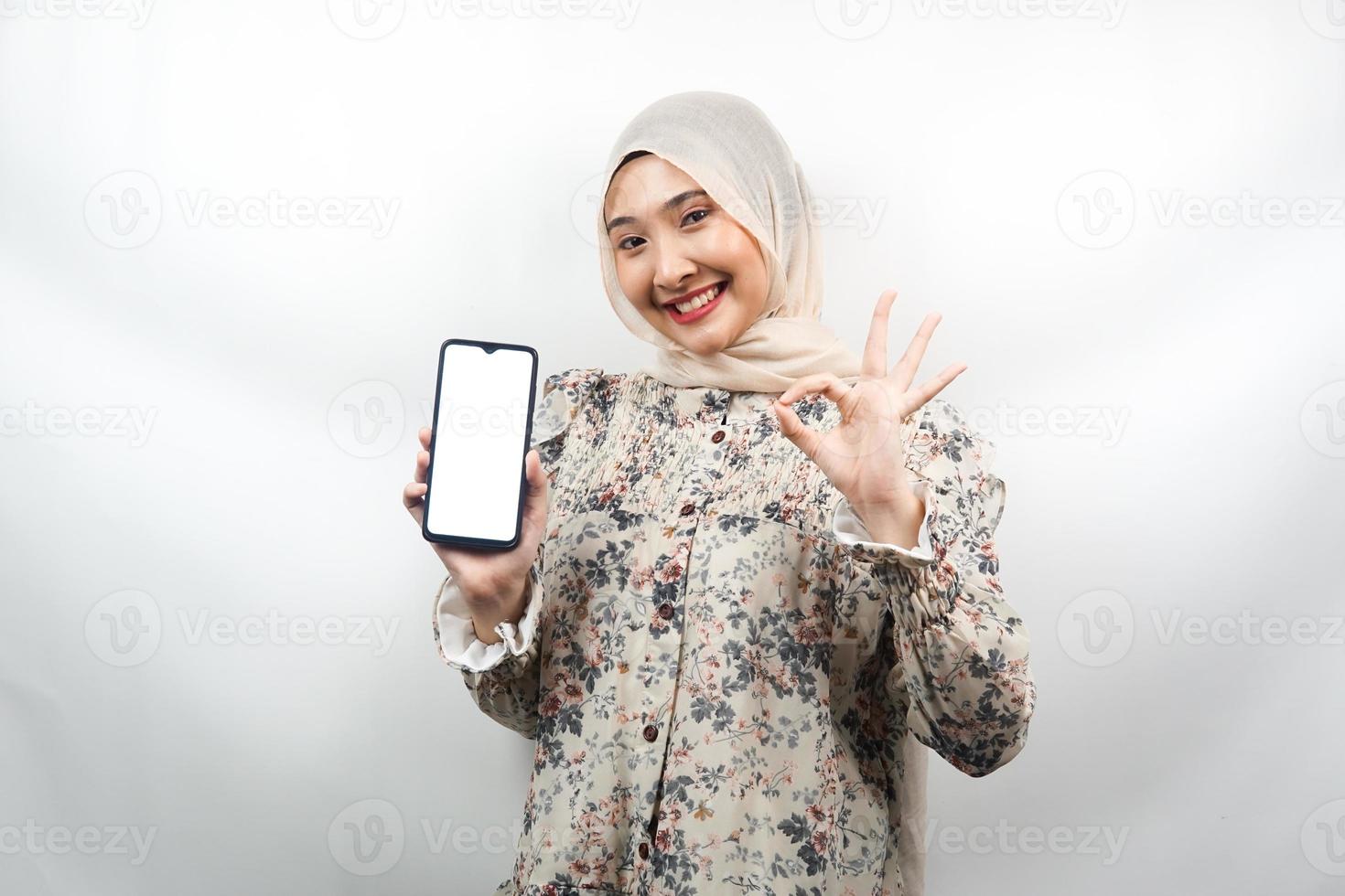 Schöne junge asiatische muslimische Frau, die selbstbewusst und aufgeregt mit den Händen lächelt, die Smartphone halten, Bewerbung fördern, ok Zeichenhand, gute Arbeit, Erfolg, isoliert auf weißem Hintergrund foto